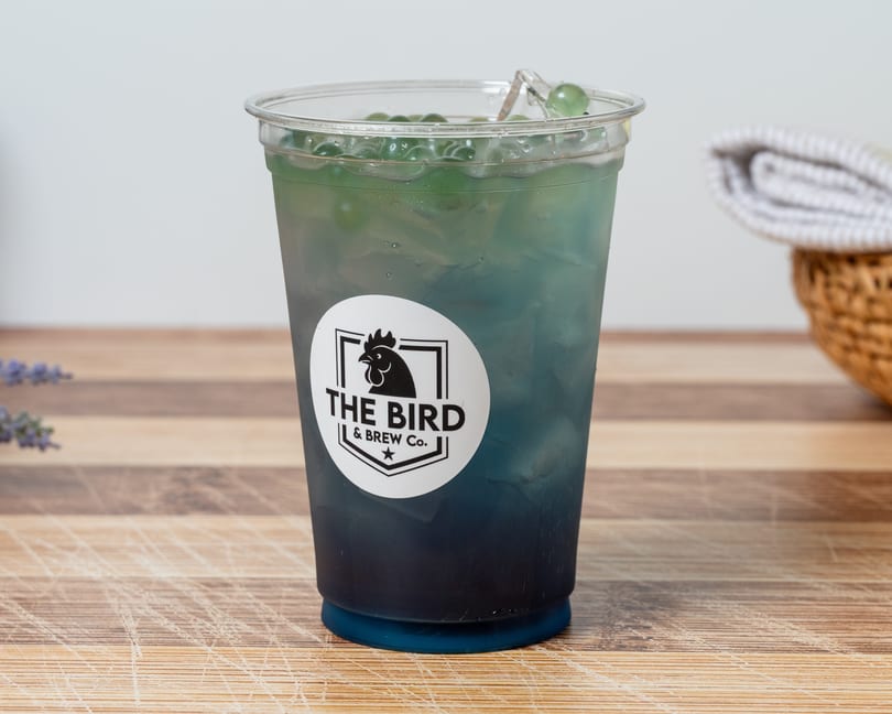A blue and green iced drink with popping boba and a "The Bird & Brew Co." logo.