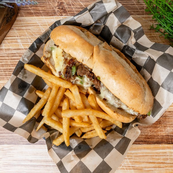 Cheesesteak sandwich with melted cheese, peppers, and onions, served with a side of fries.