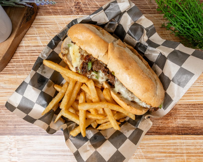 Cheesesteak sandwich with melted cheese, peppers, and onions, served with a side of fries.