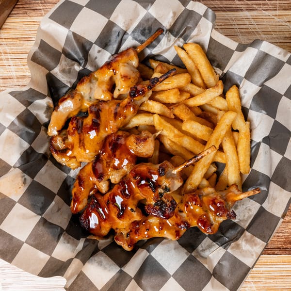 Chicken skewers with a sweet glaze and a side of golden french fries in a checkered paper basket.