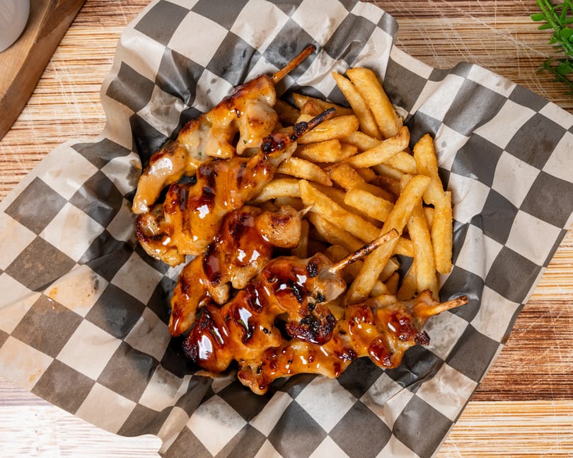 Chicken skewers with a sweet glaze and a side of golden french fries in a checkered paper basket.