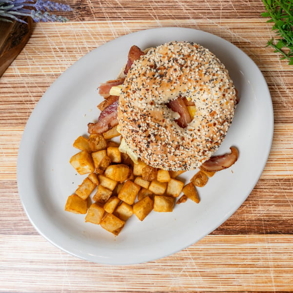 Everything bagel breakfast sandwich with bacon, egg, and cheese, served with crispy home fries.