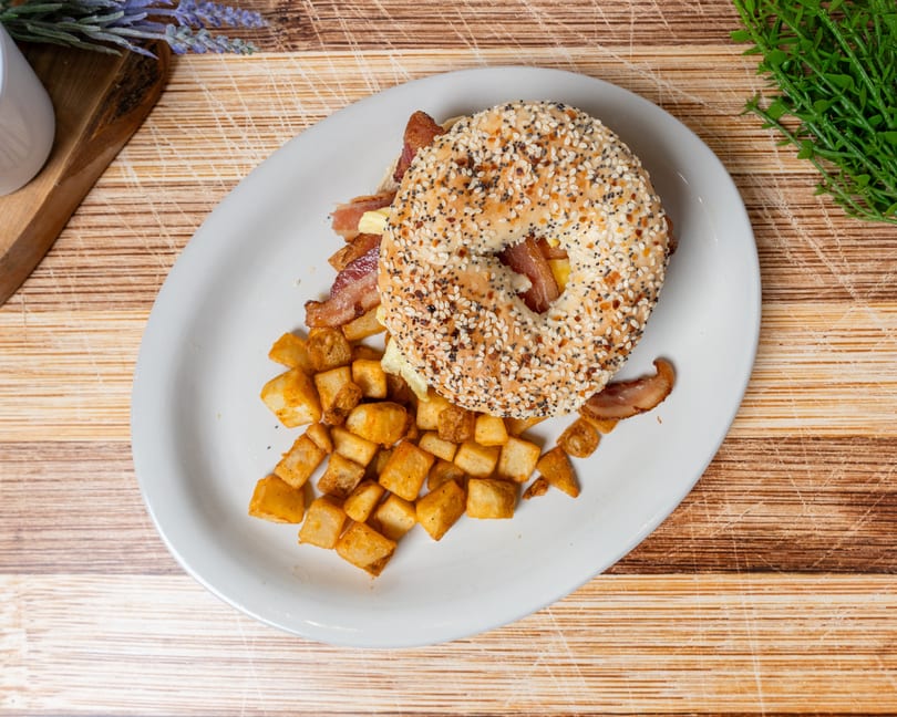 Everything bagel breakfast sandwich with bacon, egg, and cheese, served with crispy home fries.