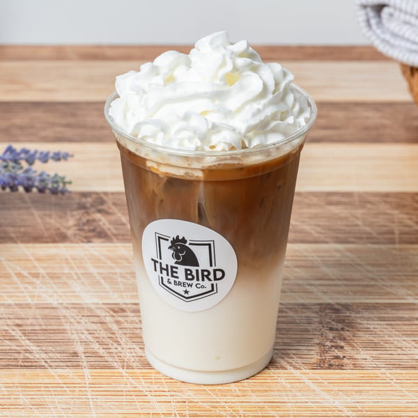 Iced coffee with whipped cream and "The Bird & Brew Co." logo on a wooden surface.