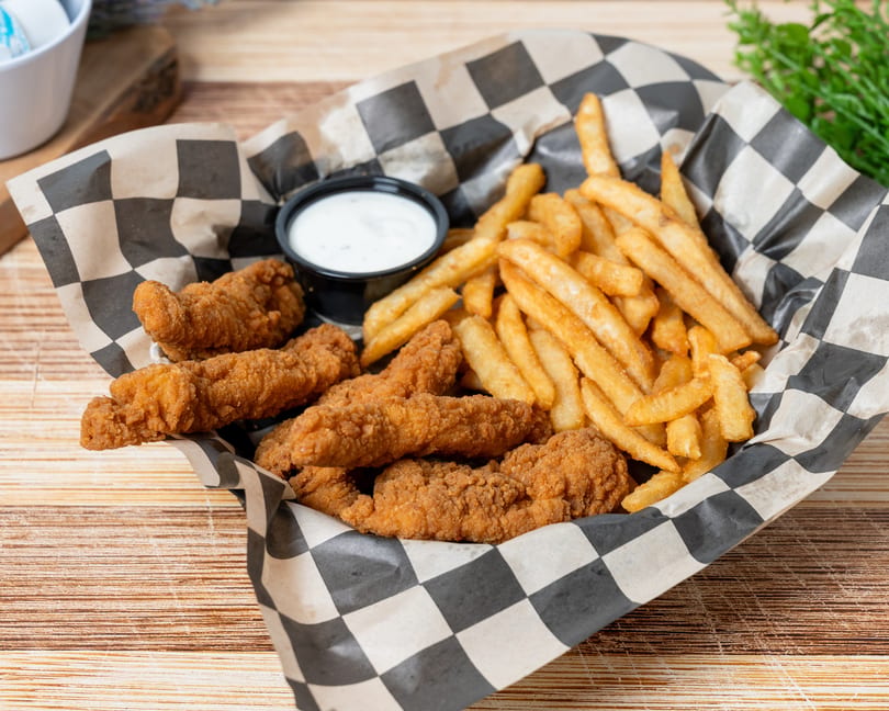 Crispy chicken tenders and golden french fries in a checkered paper-lined basket with ranch dip.