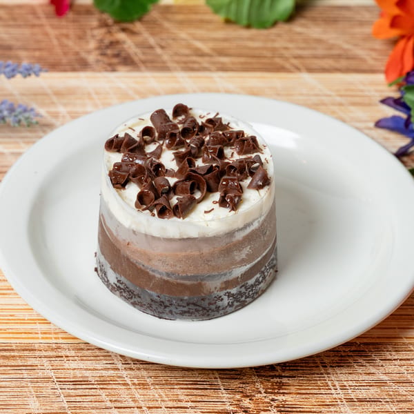 A layered chocolate dessert with white cream and chocolate curls on a white plate.
