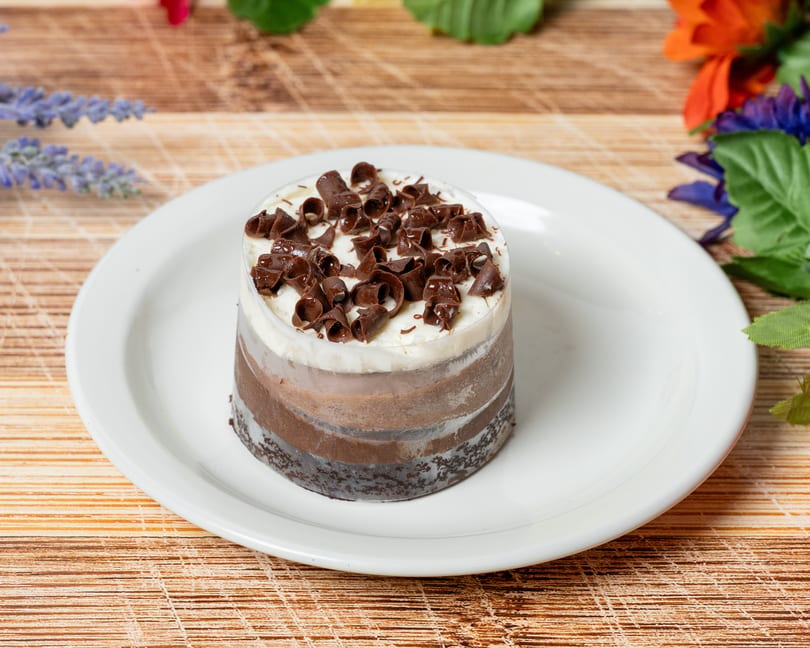 A layered chocolate dessert with white cream and chocolate curls on a white plate.