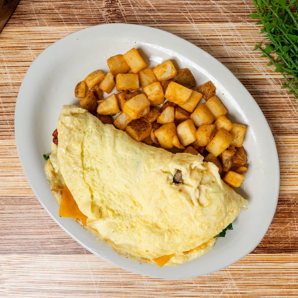 A fluffy omelet filled with cheese and spinach, served with a side of crispy home fries.