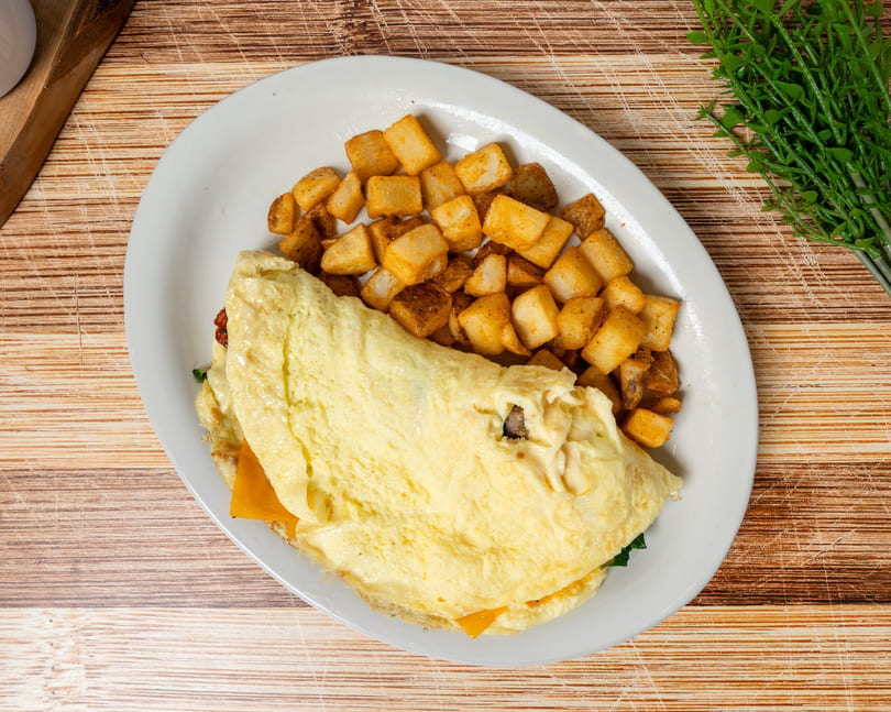 A fluffy omelet filled with cheese and spinach, served with a side of crispy home fries.