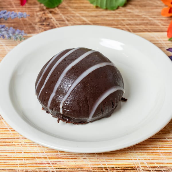 A dark chocolate dessert with white icing stripes on a white plate, on a wooden surface.